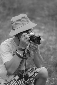 Young man wearing hat photographing on field