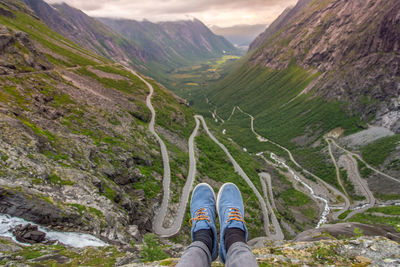 Low section of man sitting on cliff against mountains