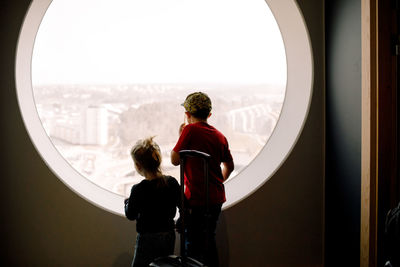 Siblings looking through window while standing in hotel room