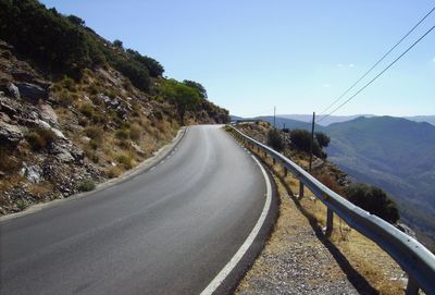 Empty road leading towards mountains against clear sky