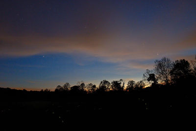 Silhouette trees on landscape against sky at sunset