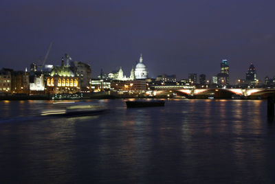 Illuminated cityscape by river against sky at night