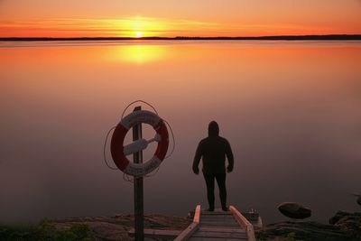 Man standing by sea against sky during sunset