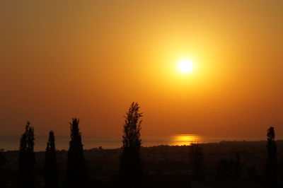 Silhouette trees on landscape against orange sky