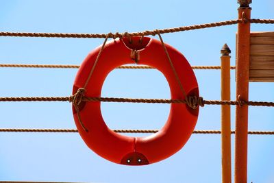 Low angle view of orange life belt hanging from ropes against clear sky