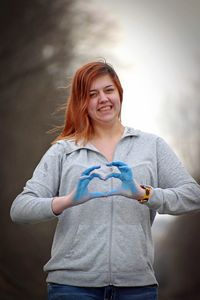 Portrait of smiling woman making heart shape outdoors