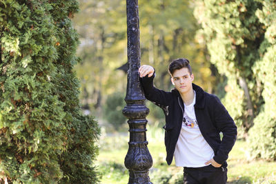 Young man looking away while standing by pole in park