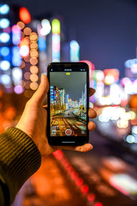 Cropped image of hand holding illuminated smart phone at night