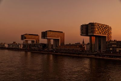 Buildings by river against sky during sunset - cologne kranhauses 