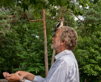 Bird perching on man head against trees