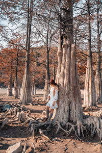 Woman standing by bare tree in forest