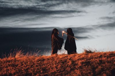 Rear view of women standing on field against sky