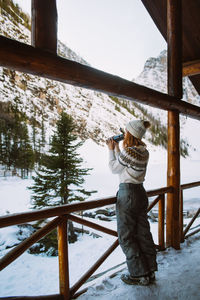 Female traveler enjoying hot drink from thermos while resting in wooden shelter near snowy mountains in banff national park