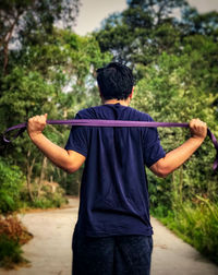 Rear view of man doing resistance band exercises against trees.