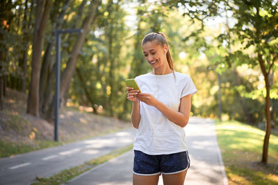 Smiling young woman using mobile phone against trees