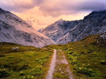 Dirt road along landscape and mountains against sky