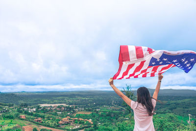 Rear view of woman holding flag against sky