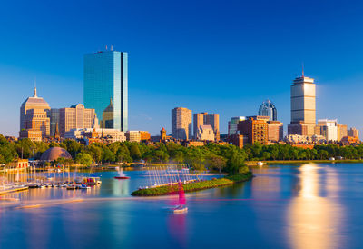 Buildings by river against clear blue sky