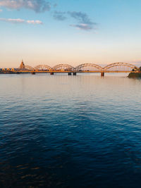 Railway bridge over daugava river against sky during sunset