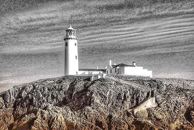 Lighthouse amidst sea and buildings against sky