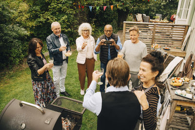 Senior men and women raising toast to party hosts at back yard