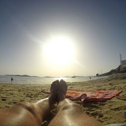 Low section of woman relaxing on beach during sunny day