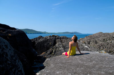 Woman on rock by sea against blue sky