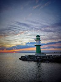 Lighthouse by sea against sky during sunset
