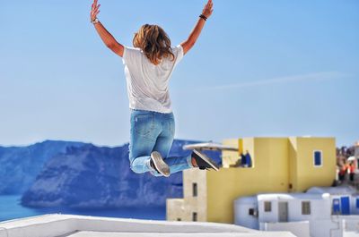 Rear view of young woman jumping against clear sky