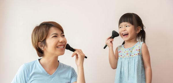 Smiling daughter and daughter applying make-up against wall at home