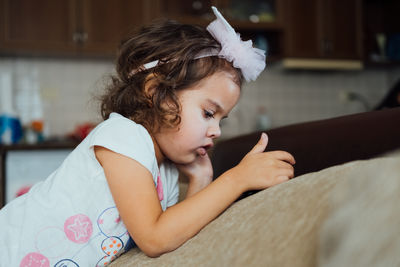 Cute little kid girl using mobile phone sitting on sofa alone small child holding phone