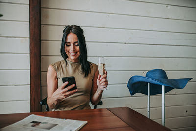 Woman using mobile phone while having wine at home