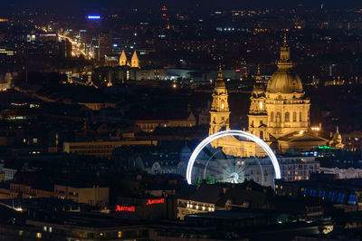 Illuminated ferris wheel by cathedral at night