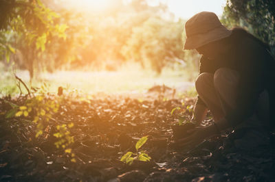 Side view of woman sitting on field during sunset