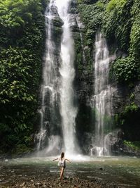 Woman standing against waterfall in forest