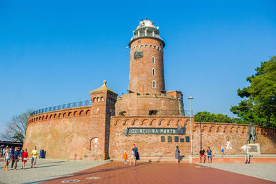 Group of people in front of historical building against blue sky