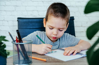 Cute little boy drawing in his notebook at the table