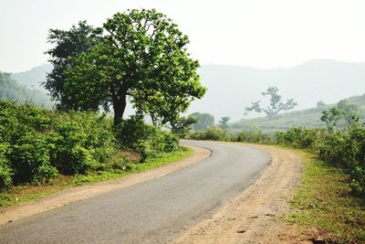 Road amidst trees on field against clear sky