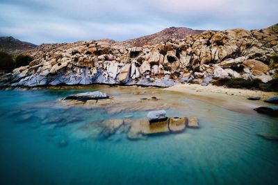 Scenic view of rocks on seashore against sky