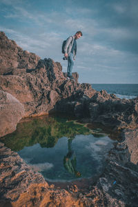 Man standing on rock by sea against sky