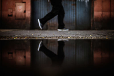 Low section of person walking by reflection in puddle at sidewalk