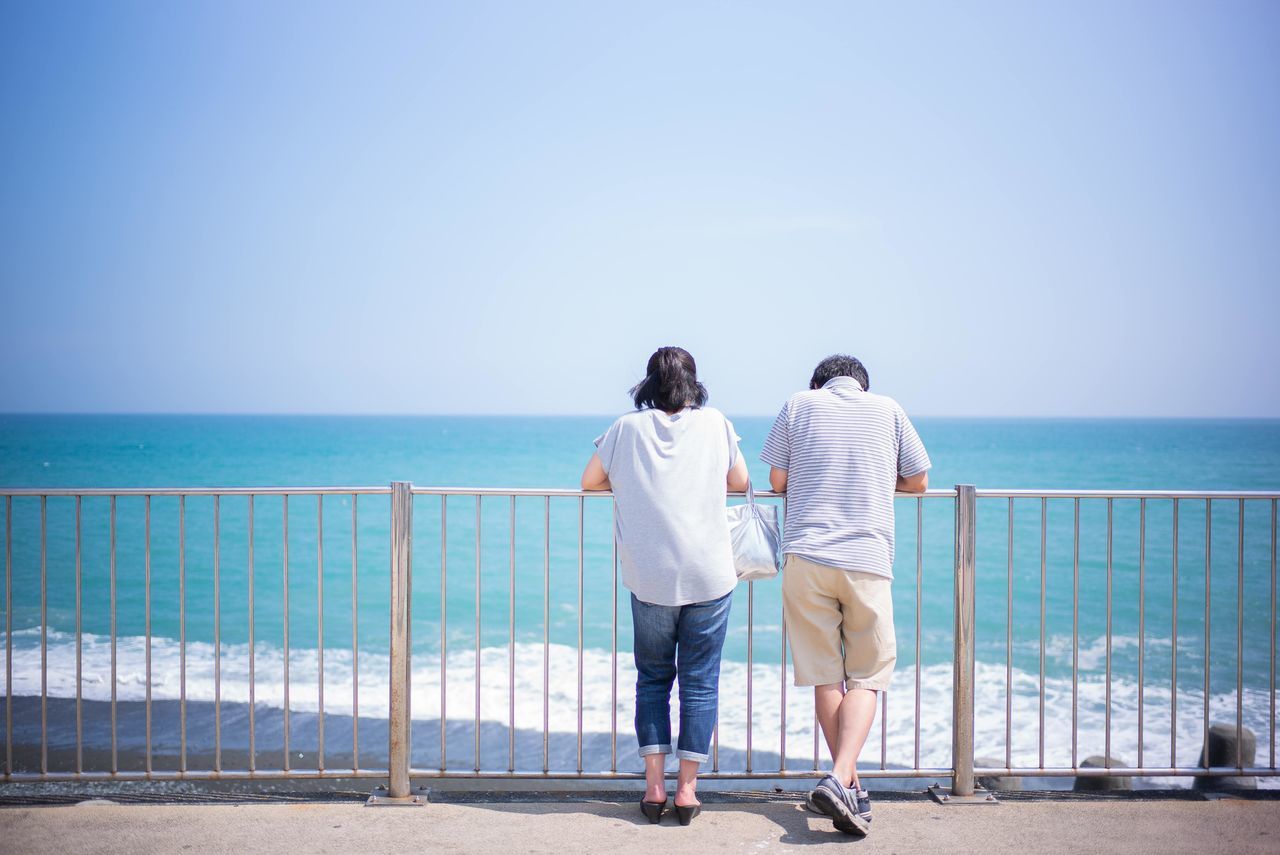 REAR VIEW OF TWO PEOPLE LOOKING AT SEA