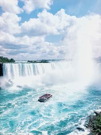 Scenic view of boat by waterfall against cloudy sky