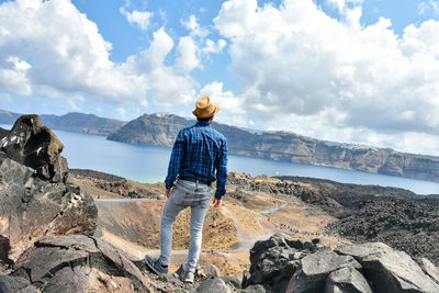 Rear view of woman standing on rock against sky