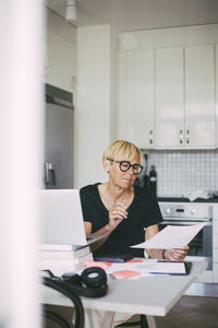 Woman working in kitchen at home reading document