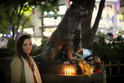 Portrait of smiling young woman standing outside animal sculpture at night