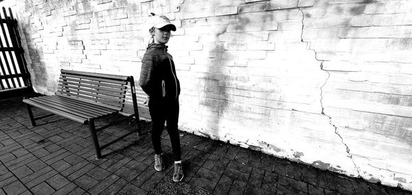 Portrait of girl standing on footpath against wall