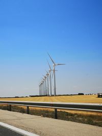 Wind turbines on field against clear blue sky