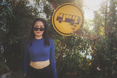 Portrait of young woman wearing sunglasses standing by trees