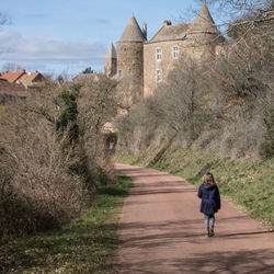 Rear view of woman walking on footpath amidst castle 